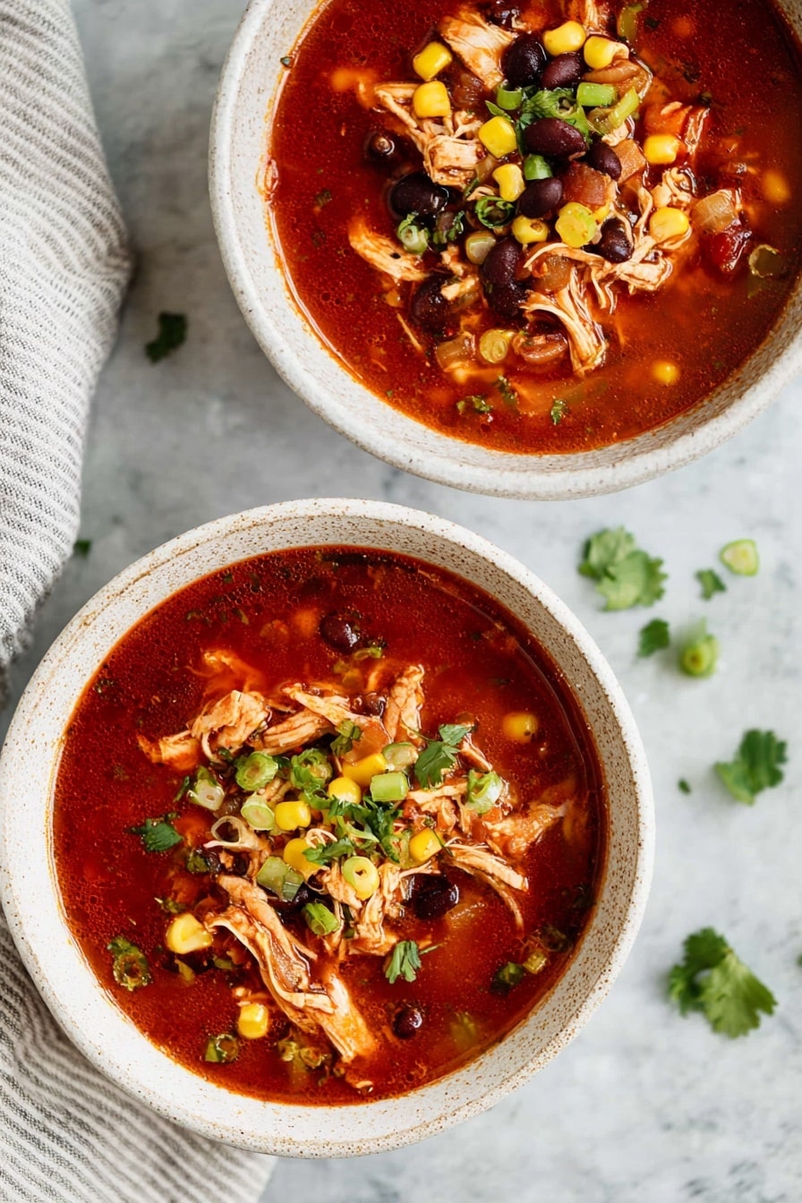 Two white speckled bowls filled with a rich red soup placed on a white marbled surface. The soup has shredded chicken pieces on top, black beans, yellow corn kernels, and small bits of green onions spread evenly in each bowl. There are also small green cilantro leaves scattered both on the soup and around the surface. A folded cloth with light gray stripes is visible in the top left corner. photo taken with an iphone --ar 2:3 --v 7 - Instant Pot Southwest Chicken Soup, Southwest Chicken Soup recipe, quick chicken soup, easy Instant Pot recipes, hearty chicken soup