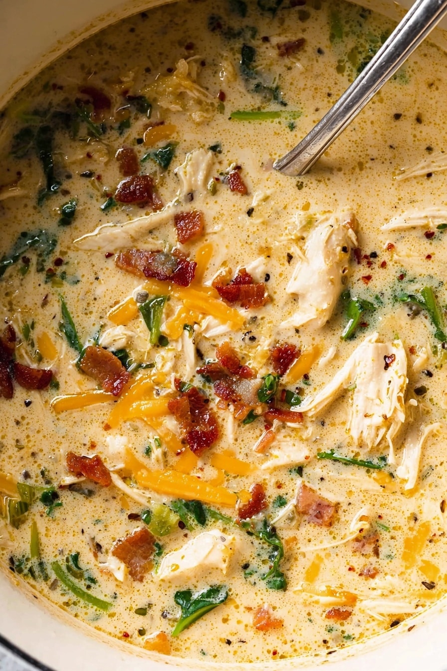 A close-up view of a creamy soup in a white pot with a silver spoon resting inside. The soup has a light beige creamy base, mixed with pieces of shredded white chicken, small bright orange cheese shreds, dark green leafy vegetables, and bits of crispy brown bacon scattered throughout. The surface shows a mix of smooth creamy texture and small seasoning specks. The soup looks thick and rich. Photo taken with an iphone --ar 2:3 --v 7 - Slow Cooker Crack Chicken Soup, cheesy chicken soup, easy chicken soup recipes, Crockpot crack chicken, hearty chicken and bacon soup