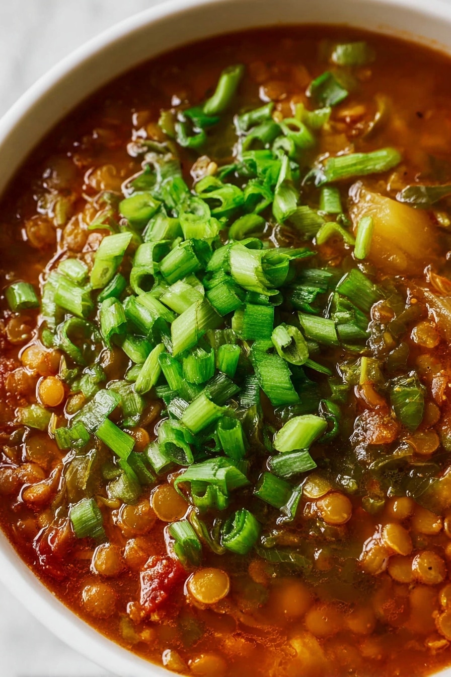 A close-up view of a bowl of soup showing two main layers: the bottom layer is a rich, reddish-brown broth filled with various lentils and small vegetable pieces, creating a textured and hearty base, while the top layer is a generous sprinkle of fresh, bright green chopped spring onions scattered evenly across the surface, adding a fresh contrast to the warm soup below. The bowl is white and placed on a white marbled surface. Photo taken with an iphone --ar 2:3 --v 7 - Slow Cooker Lentil Soup with Potatoes, Carrots, and Greens, Healthy Lentil Soup, Easy Vegetarian Soup, Cozy Lentil and Vegetable Soup, Nourishing Slow Cooker Soup