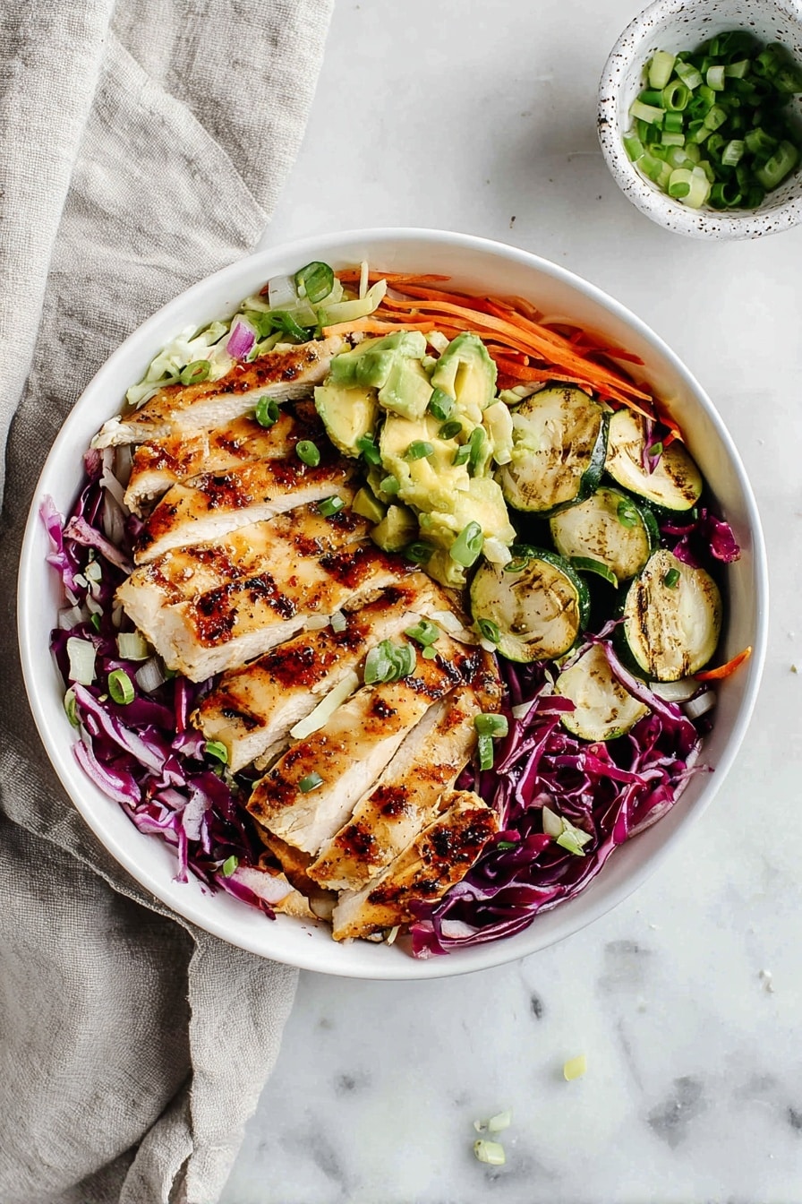 A white bowl holds a layered salad starting with a base of shredded red and white cabbage mixed with thin carrot strips, creating a colorful, textured foundation. On top, two sections of grilled chicken slices with golden brown, slightly charred grill marks are neatly arranged on opposite sides of the bowl. In the middle, pieces of grilled zucchini with charred edges sit beside small chunks of green avocado. The salad is sprinkled with chopped green onions and small pieces of red onion, adding freshness and color contrast. The bowl is placed on a white marbled surface with a light gray cloth nearby and a small white speckled cup containing extra chopped green onions in the background. Photo taken with an iphone --ar 2:3 --v 7 - Grilled Chicken and Colorful Cabbage Salad with Zucchini and Lemon Dressing, healthy chicken salad, vibrant veggie salad, quick summer chicken salad, easy grilled chicken recipes