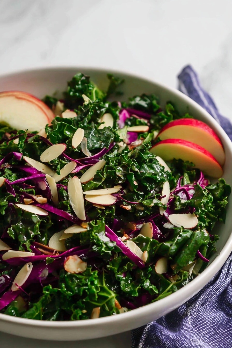 A white bowl is filled with a fresh salad made of curly dark green kale leaves and thin strips of purple cabbage mixed throughout. Thin, pale beige almond slices are scattered on top, adding texture. Near the edge of the bowl, thin slices of red apple with white flesh are partly visible, adding a hint of color contrast. The bowl sits on a white marbled surface with a blue and white striped cloth partially showing beneath it. The light highlights the fresh, natural shine of the leafy greens and nuts. photo taken with an iphone --ar 2:3 --v 7 - Chopped Red Cabbage Kale Salad with Lemon Balsamic Dressing, healthy colorful kale salad, quick vegan green cabbage salad, nutrient-rich cabbage and kale salad, tangy lemon balsamic dressing recipe