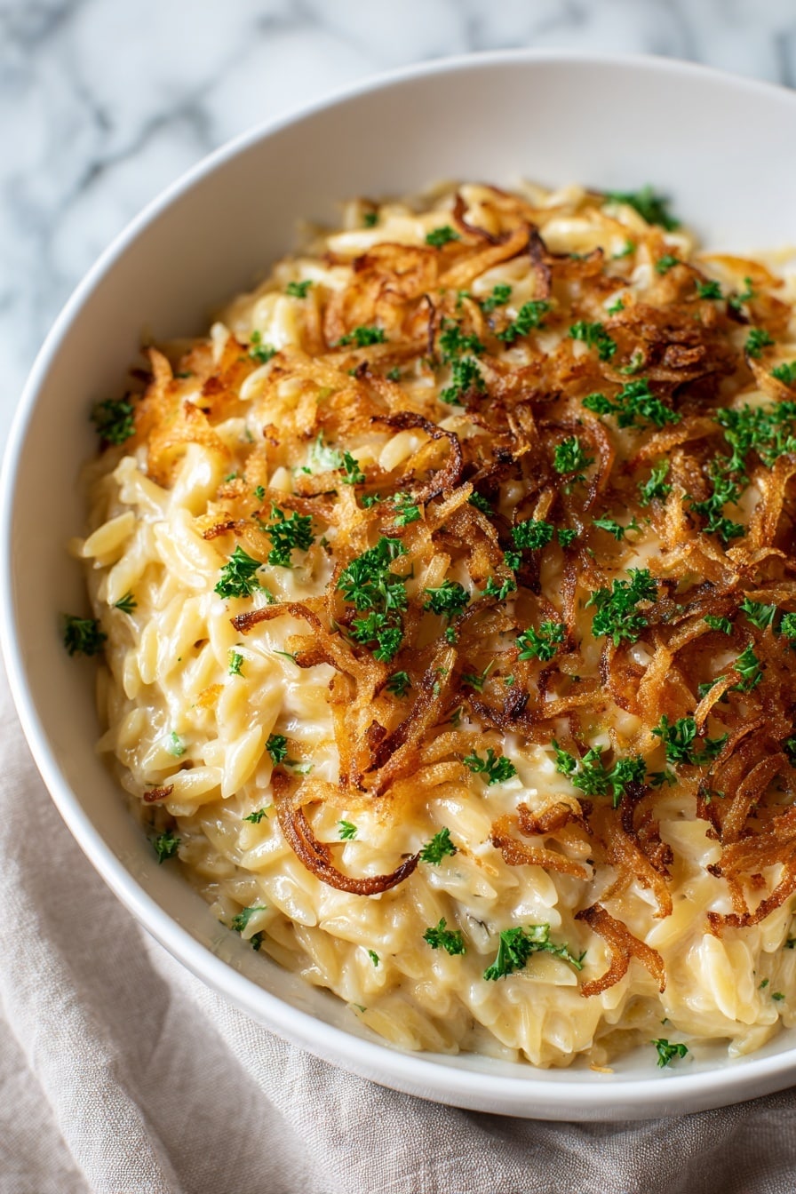 A white bowl filled with creamy, golden pasta with small tube shapes layered thickly. On the top, there is a layer of crispy, golden-brown fried onions scattered unevenly. Small green parsley pieces are spread over the onions and pasta, giving a fresh contrast. The pasta looks soft and saucy with melted cheese strings mixed through. The bowl is placed on a white marbled surface with a soft cloth underneath, creating a cozy and inviting look. Photo taken with an iphone --ar 2:3 --v 7 - French Onion Chicken Orzo Casserole, comforting chicken pasta bake, caramelized onion casserole, easy orzo casserole recipes, French onion-inspired dinner