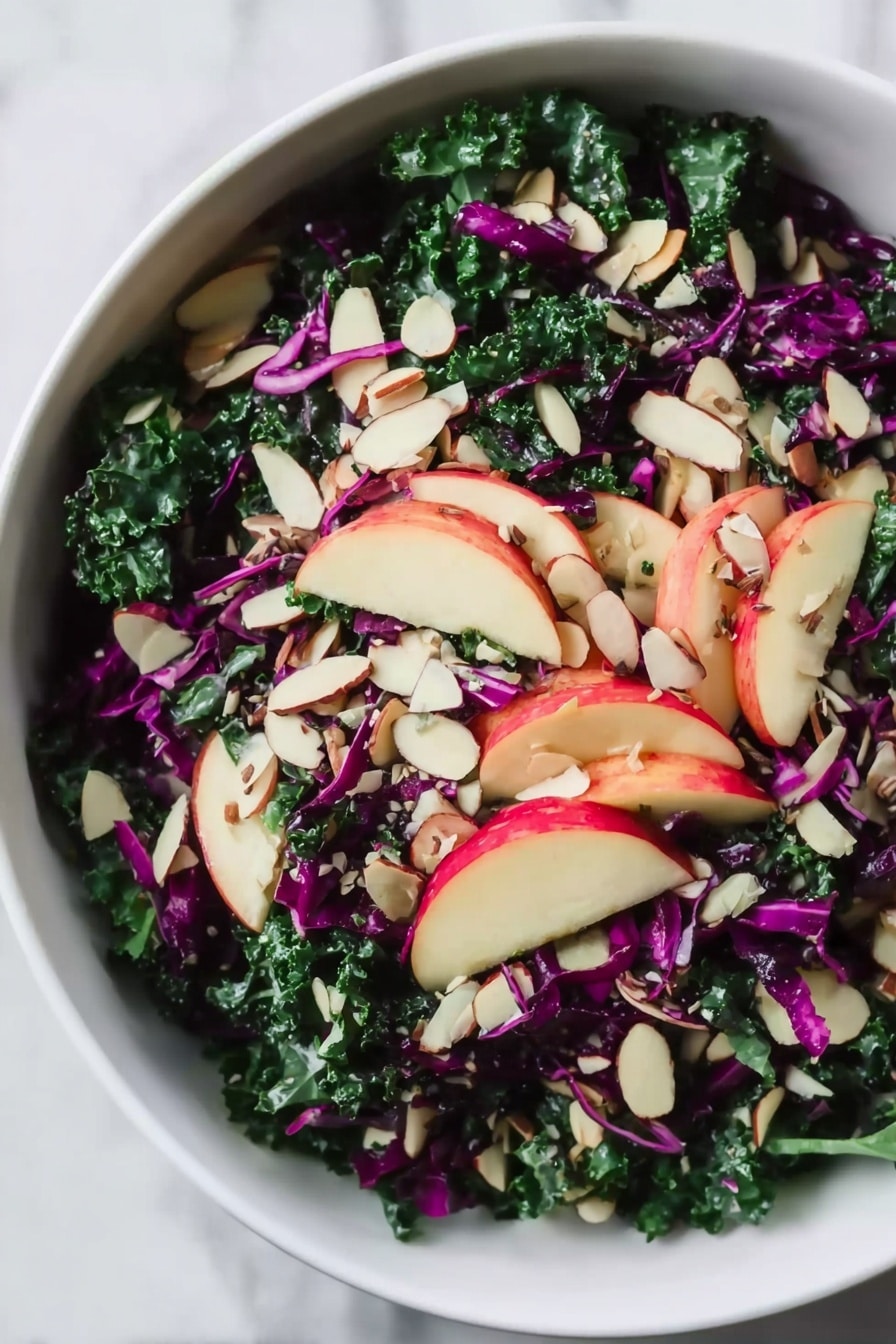 A white bowl filled with a fresh salad layered with dark green kale leaves as the base, deep purple shredded cabbage scattered throughout, and thin slices of red apple arranged on top. Light-colored almond slices are sprinkled evenly across the salad, adding texture and contrast. The bowl is placed on a white marbled surface. photo taken with an iphone --ar 2:3 --v 7 - Chopped Red Cabbage Kale Salad with Lemon Balsamic Dressing, healthy colorful kale salad, quick vegan green cabbage salad, nutrient-rich cabbage and kale salad, tangy lemon balsamic dressing recipe