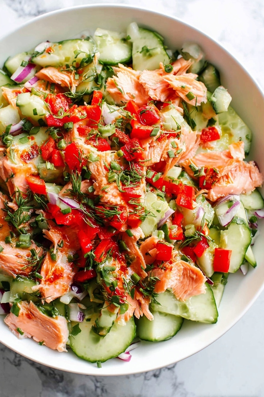 The dish is a fresh salad served in a white bowl with one main layer made of mixed ingredients. The base layer shows thinly sliced cucumber pieces with dark green edges and light green centers spread across the bowl. Bright red bell pepper chunks are scattered evenly over the cucumbers. Shredded orange-pink salmon pieces are placed on top, with some small bits of red onion slices visible between the other items. Fresh chopped green herbs are sprinkled over the entire salad, adding a bright green accent. The whole bowl rests on a white marbled surface with a light texture and subtle veins. Photo taken with an iphone --ar 2:3 --v 7 - Chopped Salmon Salad, healthy salmon salad, quick salmon salad recipe, fresh seafood salad, easy salmon salad ideas