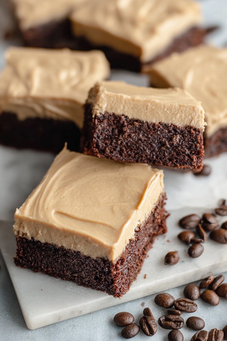 The image shows several square brownies with two layers: the bottom layer is dark brown and fudgy, while the top layer is smooth and light tan frosting spread evenly. The brownies rest partly on a white plate with some placed directly on a white marbled surface sprinkled with dark roasted coffee beans. The frosting has subtle swirls giving it a slightly textured look. The scene is close up, focusing on the details of the layers and textures. Photo taken with an iphone --ar 2:3 --v 7 - Frosted Coffee Brownies, coffee brownies, chocolate coffee dessert, fudgy coffee brownies, easy coffee brownies