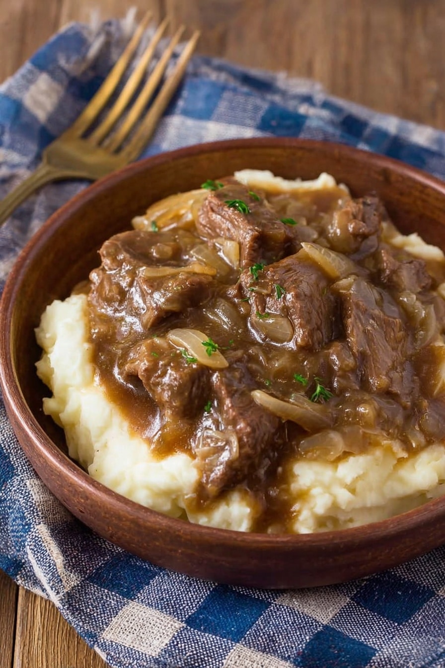 A rustic brown bowl holds two main layers: the bottom layer is creamy white mashed potatoes with a smooth and soft texture, while the top layer is a rich, dark brown beef stew with chunks of tender beef and translucent cooked onions mixed in a thick gravy. The bowl is placed on a wooden surface partially covered by a blue and white checkered cloth, and a brass fork rests nearby. Photo taken with an iphone --ar 2:3 --v 7 - Instant Pot French Onion Pot Roast, French Onion Pot Roast, Instant Pot Beef Roast, Easy French Onion Pot Roast, Slow Cooker French Onion Roast