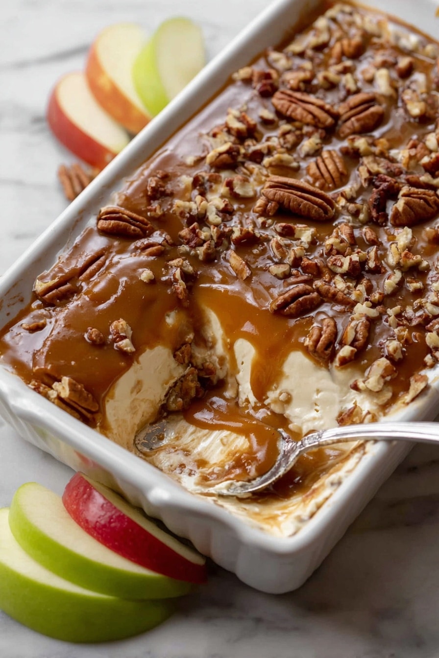 A white rectangular dish holds a dessert with three layers: the bottom layer is light cream color and smooth, the middle layer is a thin sticky caramel, and the top layer is dark caramel brown topped with chopped pecans scattered evenly. A spoon in the dish scoops some of the dessert, showing the soft creamy texture inside. Green and red apple slices sit beside the dish on a white marbled surface. Photo taken with an iphone --ar 2:3 --v 7 - Caramel Apple Cheesecake Dip, easy caramel apple dip, apple dessert dip, no-bake cheesecake dip, fall appetizer recipes
