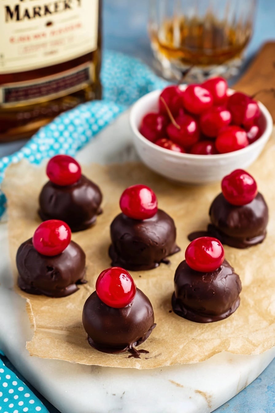 The image shows seven small round chocolate-covered treats each topped with a shiny red cherry. They are placed on light brown parchment paper on a white marbled surface with a light blue cloth with blue polka dots nearby. In the background, there is a small white bowl filled with bright red cherries and a blurred bottle of whiskey on a wooden board. The chocolate coating is smooth but slightly uneven, with the cherries positioned on top, adding a pop of glossy red color on each dark brown sweet. Photo taken with an iphone --ar 2:3 --v 7 - Cherry Bourbon Balls, Bourbon Christmas Treats, Cherry Candy Balls, Easy Bourbon Confections, Holiday Party Bites