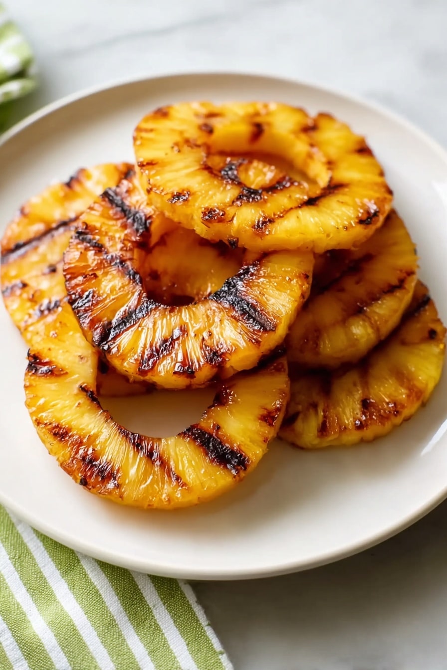 The image shows a white plate with five grilled pineapple rings stacked in a loose pile, each ring bright yellow with golden caramelized edges and dark brown grill marks running across them. The pineapple texture looks juicy and slightly translucent, with the charred lines adding contrast to the soft fruit surfaces. The plate sits on a white marbled surface with a green and white striped cloth partially visible at the bottom left corner. The lighting highlights the shiny, grilled fruit, giving a fresh and warm look photo taken with an iphone --ar 2:3 --v 7 - Grilled Pineapple with Lime and Coconut, tropical grilled pineapple, pineapple dessert ideas, summer fruit recipes, easy grilled pineapple