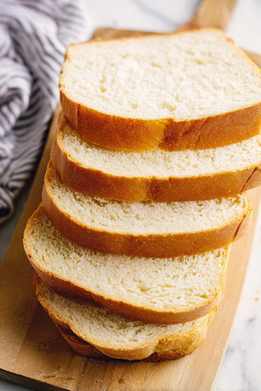 A close-up view of five slices of light golden brown bread stacked slightly tilted on a wooden board. Each slice shows a soft, fluffy white inside with a thin, smooth crust. The wooden board rests on a white marbled surface, and a blurred striped cloth is visible in the background. Photo taken with an iphone --ar 2:3 --v 7 - White Sandwich Bread, homemade bread recipe, fluffy bread loaf, easy bread baking, soft sandwich bread