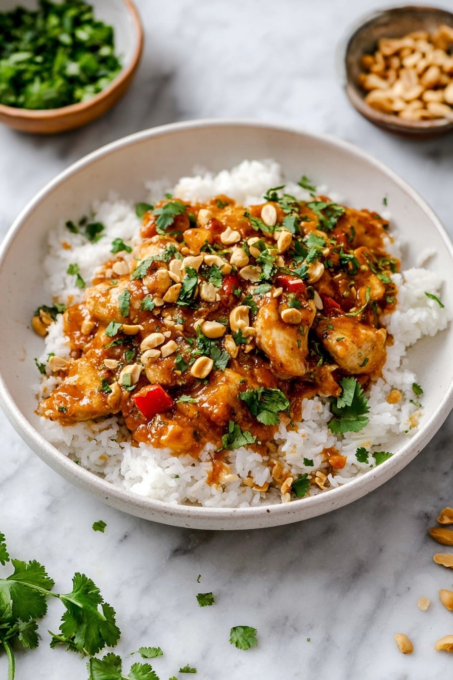A white bowl holds a base layer of fluffy white rice with a slightly sticky texture, topped with pieces of light brown cooked chicken covered in a thick, glossy, orange-brown sauce with visible small chunks of red pepper. Scattered on top are chopped peanuts adding a crunchy texture and green cilantro leaves sprinkled around for a fresh touch. The bowl is placed on a white marbled surface with two small bowls nearby, one filled with chopped green herbs and the other with peanuts. Some cilantro leaves are scattered on the surface near the bowl. Photo taken with an iphone --ar 2:3 --v 7 - Slow Cooker Peanut Chicken, easy slow cooker chicken recipes, creamy peanut chicken, flavorful chicken dinner, weeknight slow cooker meals