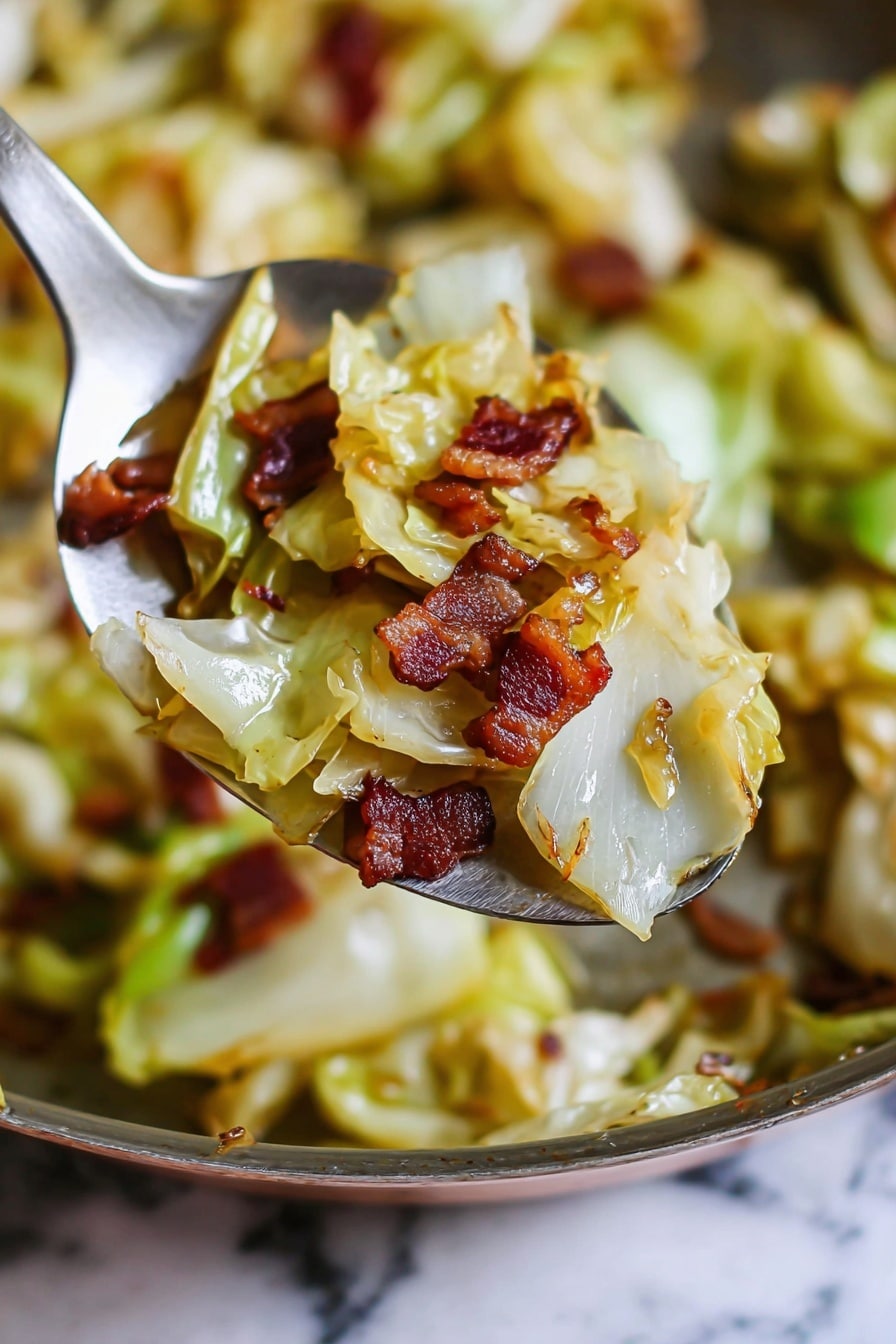 The image shows a close-up of a metal spoon holding a mix of cooked cabbage and small pieces of crispy bacon. The cabbage pieces are light green and yellow with a soft, slightly shiny texture. The bacon pieces are deep reddish-brown, adding a crunchy contrast to the tender cabbage. The background shows more of the cooked cabbage and bacon in the pan with a warm golden-brown tone. The overall visual is warm and appetizing, focused on the mixture held by the spoon. The surface beneath is a white marbled texture. Photo taken with an iphone --ar 2:3 --v 7 - Easy Fried Cabbage, fried cabbage side dish, crispy bacon cabbage, quick cabbage recipes, comforting vegetable side