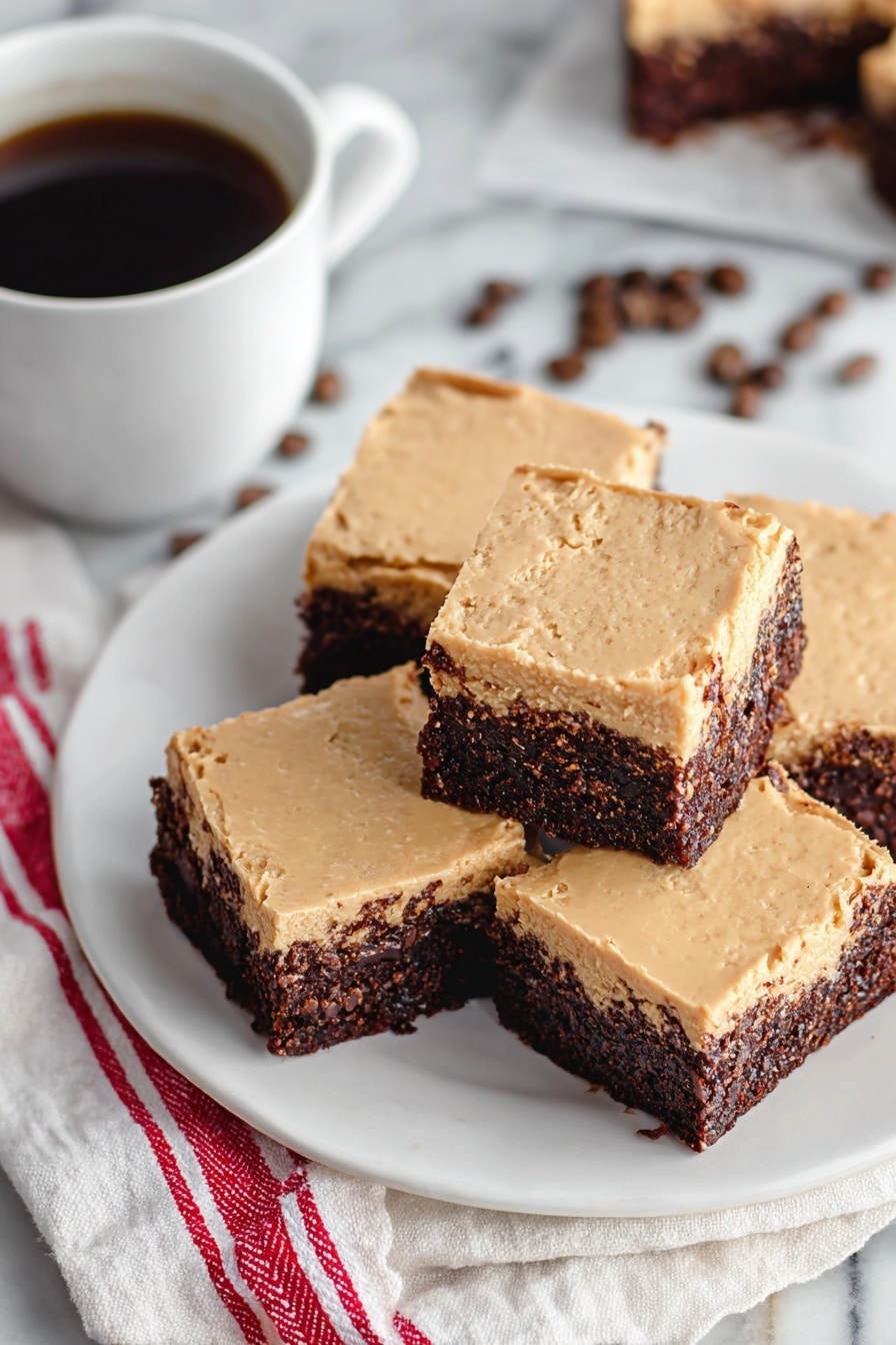 There is a white plate with five square brownies stacked on it. Each brownie has two layers: a dark brown, moist-looking bottom layer and a light brown, creamy top layer that appears smooth but slightly textured. The plate is placed on a white marbled surface with a folded white cloth that has red stripes beneath part of it. In the background, to the left, there is a white cup filled with dark coffee and a few coffee beans scattered nearby. Photo taken with an iphone --ar 2:3 --v 7 - Frosted Coffee Brownies, coffee brownies, chocolate coffee dessert, fudgy coffee brownies, easy coffee brownies