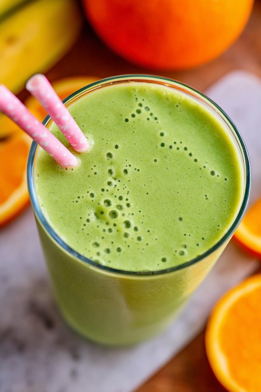 A clear glass filled with one layer of light green smoothie that has a smooth but slightly bubbly texture on top. A pink and white striped straw leans into the smoothie from the left side of the glass. Around the glass, there are some orange slices and a whole orange in the background, all placed on a white marbled surface. The image is taken close up, focusing on the top of the glass, showing the smooth and creamy surface of the green drink. Photo taken with an iphone --ar 2:3 --v 7 - Green Orange Julius Smoothie, healthy green orange smoothie, citrus spinach smoothie, quick nutritious smoothie, vegan orange smoothie