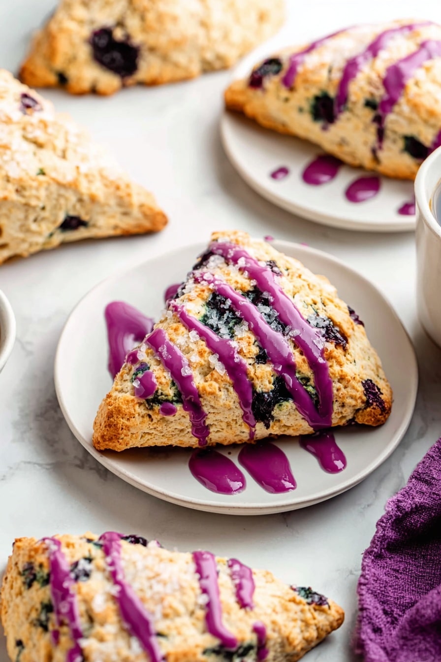 The image shows three thick, triangular blueberry scones stacked on a white marble surface, with the top scone generously drizzled with bright purple icing that contrasts with the golden brown and crumbly texture of the scones filled with dark blueberries. In the background, more scones are cooling on a wire rack, some plain and others with the same purple drizzle. To the right, there is a clear glass bottle half filled with milk, adding a fresh touch to the scene. The foreground shows part of a white plate with another scone topped with the purple icing. The overall colors are warm golden tones mixed with deep purples and white, with a soft natural light highlighting the texture of the scones. photo taken with an iphone --ar 2:3 --v 7 - Maine Wild Blueberry Scones, Blueberry Scone Recipe, Fresh Blueberry Scones, Flaky Blueberry Scones, Homemade Blueberry Scones