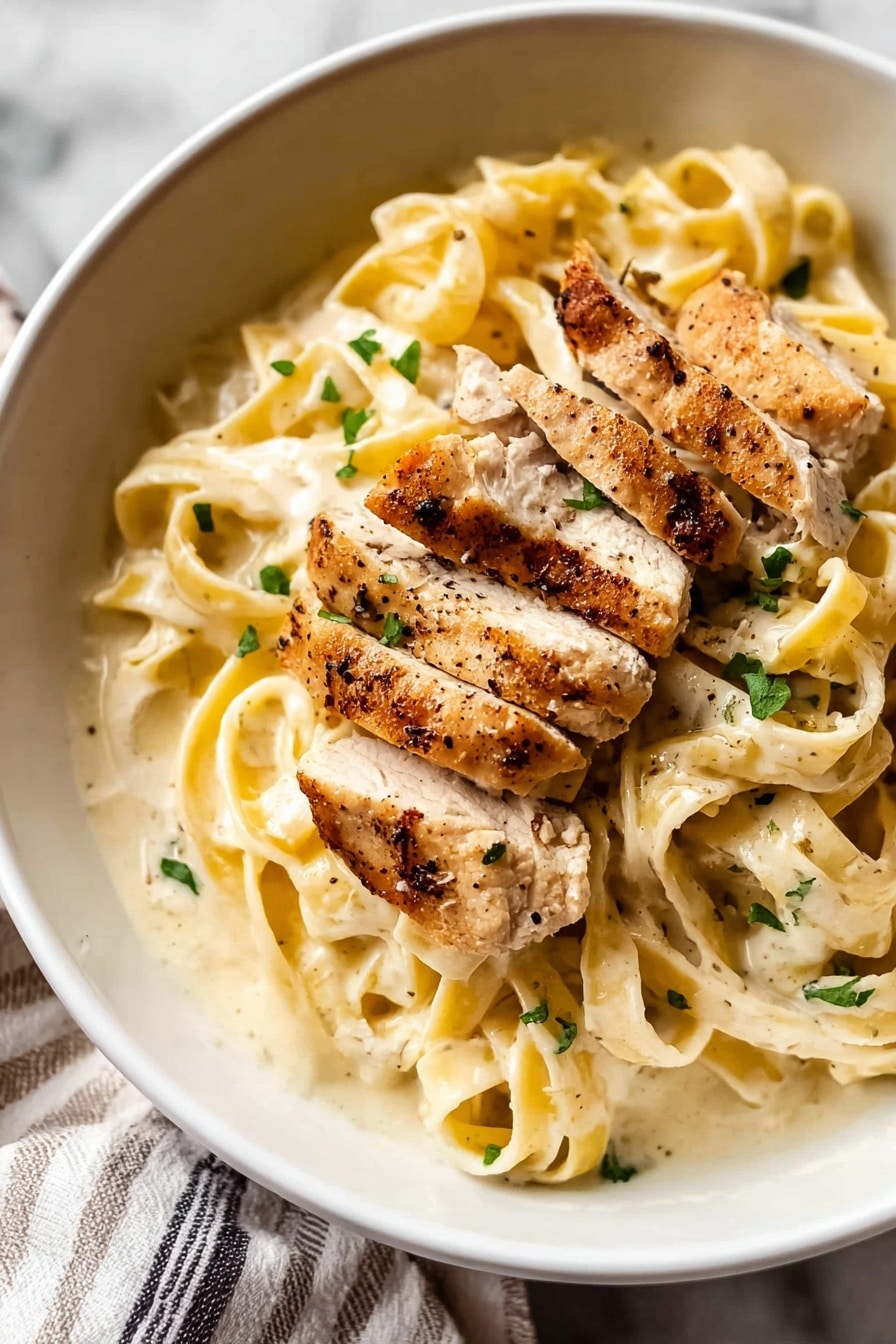 A white bowl holds a creamy pasta dish with about two layers visible: the bottom layer is wide, flat fettuccine noodles covered in a smooth, light cream sauce speckled with small green herb pieces, likely parsley. On top, there are several pieces of golden-brown cooked chicken strips, showing light seasoning with visible black pepper and herbs. The chicken pieces are placed unevenly, adding texture and depth. The bowl sits on a white marbled surface with a soft striped fabric visible at the edge. photo taken with an iphone --ar 2:3 --v 7 - Chicken Fettuccine Alfredo, easy Alfredo pasta, creamy chicken pasta, homemade Alfredo sauce, Italian chicken pasta