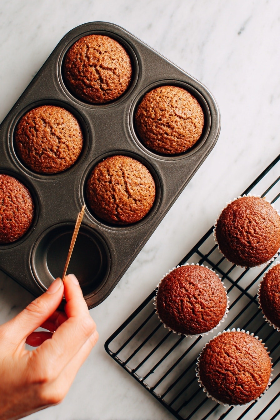 The image shows two parts of the baking process for small brown muffins. On the left side, five muffins with cracked tops are in a dark metal muffin tray, with a woman's hand holding a toothpick above one muffin to check doneness. The muffins have a textured, slightly crispy surface and a golden brown color. On the right side, the muffins are upside down on a black cooling rack, showing their flat bottom side with a more uniform dark brown look. The background is a white marbled surface. Photo taken with an iphone --ar 2:3 --v 7 - Sticky Toffee Pudding with Butterscotch Sauce, best sticky toffee pudding, easy to make sticky toffee pudding, delicious toffee pudding recipe, comfort dessert recipes