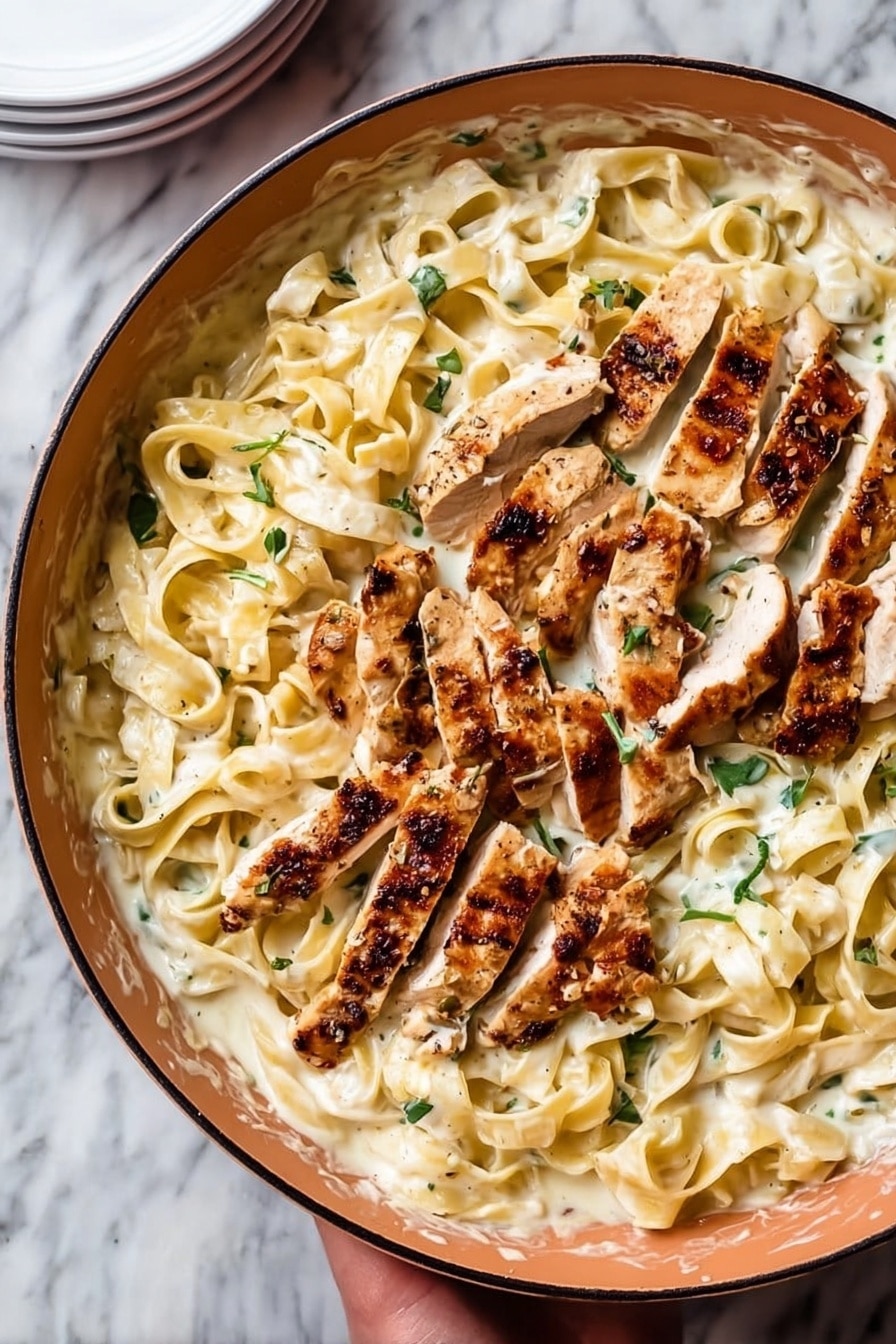 The image shows a white pan filled with wide, flat noodles covered in creamy white sauce with green herb bits mixed in. On top of the noodles are several pieces of grilled chicken, sliced into strips with a light brown color and visible grill marks. The chicken strips are spread mostly in the center and top of the pan. Small green herb leaves are scattered on the noodles and chicken. The pan is set on a white marbled surface next to a stack of white plates. A woman's hand is holding the pan from the bottom edge. Photo taken with an iphone --ar 2:3 --v 7 - Chicken Fettuccine Alfredo, easy Alfredo pasta, creamy chicken pasta, homemade Alfredo sauce, Italian chicken pasta