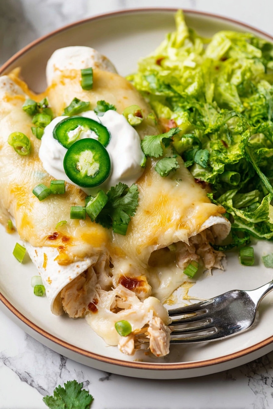 The dish shows two soft rolled tortillas filled with light brown cooked chicken pieces, topped with melted cheese that is creamy white and a bit yellow, covering the wraps fully. On top of the tortillas, there is a small dollop of smooth white sour cream with two dark green sliced jalapeños placed neatly. Around the chicken wraps, there are fresh bright green chopped scallions and green cilantro pieces scattered. On the right side of the plate, there is a pile of shredded dark green leafy lettuce. A silver fork is resting near the lettuce with one bite-sized piece on it. The food is served on a white plate with a faint brown rim, placed on a white marbled surface. Photo taken with an iphone --ar 2:3 --v 7 - White Chicken Enchiladas with Rotisserie Chicken, easy chicken enchiladas, creamy green chili enchiladas, weeknight chicken dinner, cheesy chicken enchiladas