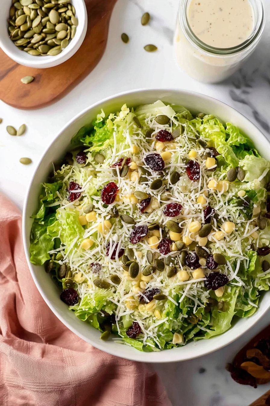 A white bowl filled with fresh green leafy lettuce as the base layer, topped with pale yellow corn kernels and thin shreds of white cheese scattered all over. The salad is garnished with small green pumpkin seeds and dark red dried cranberries spread mostly on the top. Around the bowl are a small white bowl of pumpkin seeds, a wooden board, a small glass jar of light creamy dressing, and a soft pink cloth, all placed on a white marbled surface. photo taken with an iphone --ar 2:3 --v 7 - Basil Couscous Salad, healthy couscous salad, fresh herb salad, easy Mediterranean salad, vegetarian couscous dish