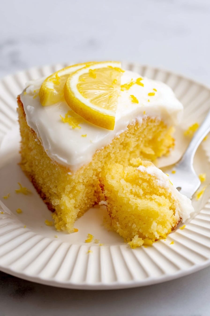 A piece of yellow lemon cake with a soft, crumbly texture sits on a white plate with ridged edges. The cake has one thick layer topped with smooth white frosting that has a creamy look. On top of the frosting, there is a thin lemon slice placed near the edge with a few lemon zest sprinkles scattered around. A small bite is taken out of the cake, and a white fork with a piece of the cake is lying nearby on the plate. The scene is set on a white marbled surface. photo taken with an iphone --ar 2:3 --v 7 - Bright and Sunny Lemonade Cake, Lemonade Cake, Lemon Cake with Frosting, Citrus Dessert Recipes, Easy Lemon Cake