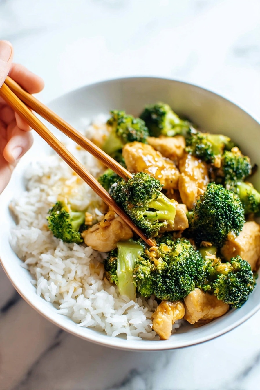 A white bowl filled halfway with white rice as the base layer, topped with vibrant green broccoli florets scattered across, mixed with light golden brown small chicken pieces cooked in sauce. A pair of wooden chopsticks held by a woman's hand is picking up one piece of chicken, slightly lifted above the bowl. The background has a white marbled texture. photo taken with an iphone --ar 2:3 --v 7 - Easy Chicken Broccoli Stir Fry, Chicken and Broccoli Stir Fry, Healthy Chicken Stir Fry, Quick Dinner Recipes, Asian Stir Fry