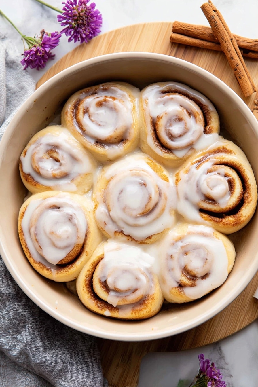 The image shows seven cinnamon rolls in a round gray pan on a white marbled surface. Each cinnamon roll has a thick spiral shape with layers of soft dough in light beige color and dark brown cinnamon filling spiraled inside. The rolls are partly covered with a creamy white glaze that looks smooth and slightly shiny, drizzled unevenly over the top and between the rolls. The rolls are packed close together, filling the pan with some rolls touching each other. A soft, light cloth is partially visible near the pan. photo taken with an iphone --ar 2:3 --v 7 - Cottage Cheese Cinnamon Rolls with Maple Glaze, Homemade cinnamon rolls, Easy cinnamon roll recipes, Soft cinnamon rolls with cottage cheese, Maple glaze cinnamon pastry