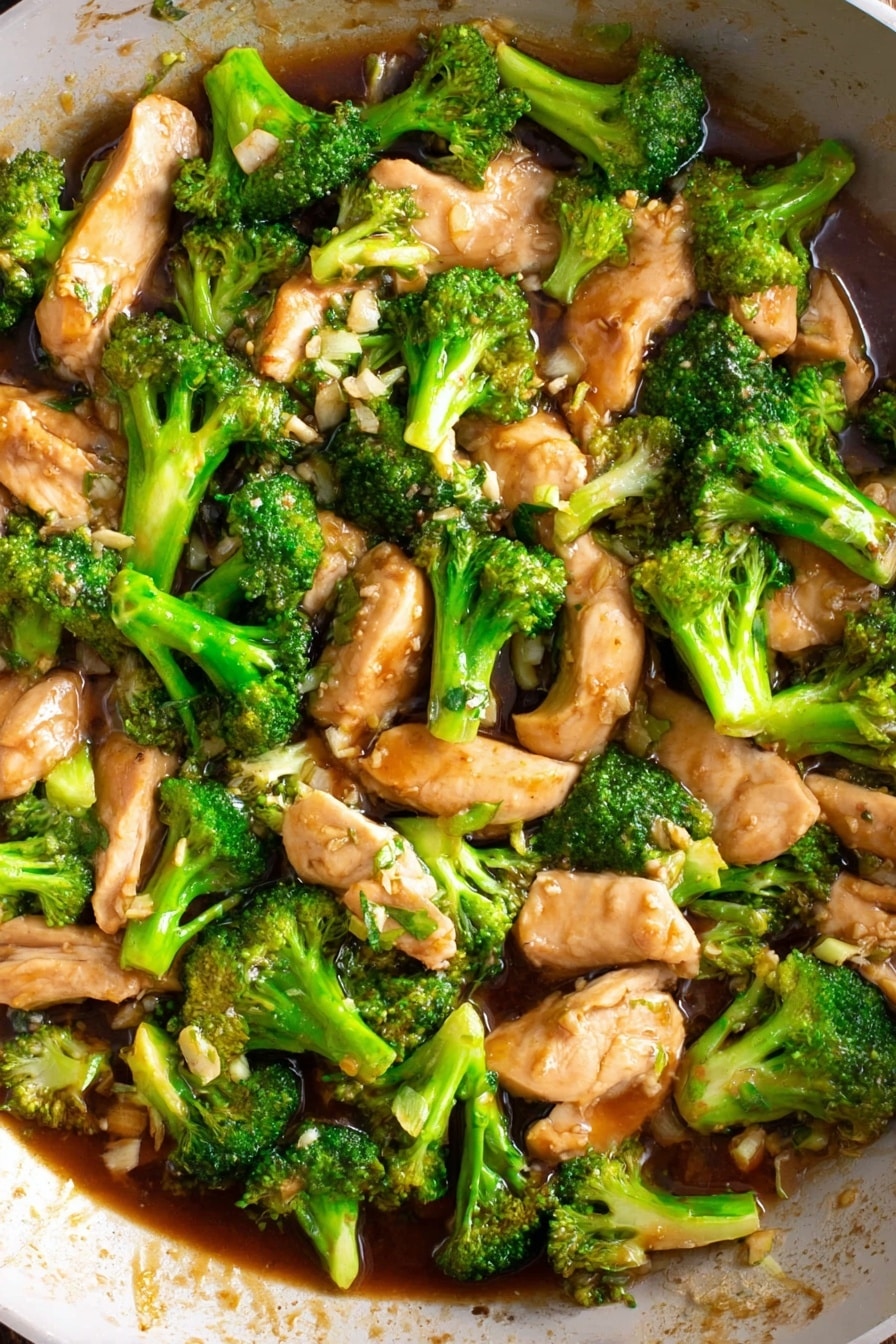 This image shows a dish of cooked broccoli and sliced chicken pieces in a brown sauce. The broccoli pieces are bright green with visible florets and stems, scattered evenly among the pale beige chicken slices. The sauce is glossy and thick, pooling slightly around the ingredients, adding a rich sheen. The dish is presented in a pan with a white marbled surface edge visible, with small bits of garlic or onion mixed into the sauce for texture. Photo taken with an iphone --ar 2:3 --v 7 - Easy Chicken Broccoli Stir Fry, Chicken and Broccoli Stir Fry, Healthy Chicken Stir Fry, Quick Dinner Recipes, Asian Stir Fry