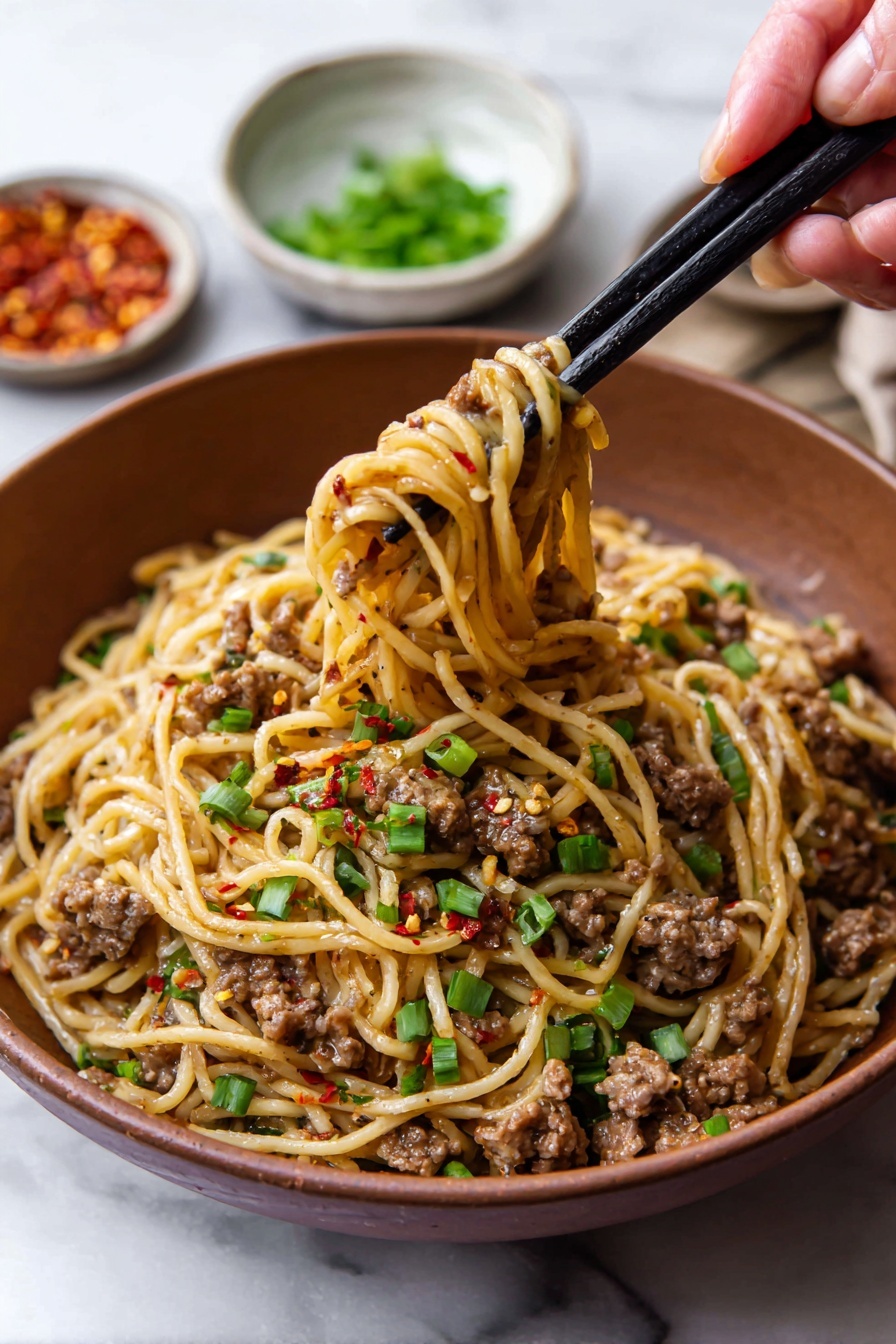 Mongolian Ground Beef and Udon Noodles Recipe 7 A brown bowl is filled with a mix of light golden noodles and small pieces of cooked brown meat, scattered with green chopped green onions and red chili flakes on top. A woman's hand holding black chopsticks lifts a tangled bite of noodles and meat from the bowl. In the background, there are small white bowls with green onions and red chili flakes on a white marbled surface. The colors are warm, with the noodles and meat showing a soft gloss, and the green onions adding freshness to the dish photo taken with an iphone --ar 2:3 --v 7 - Mongolian Ground Beef and Udon Noodles, Mongolian Beef Udon Stir-fry, Quick Asian Ground Beef Noodle Bowl, Savory Udon Noodles with Ground Beef, Easy Mongolian Beef and Udon Recipe