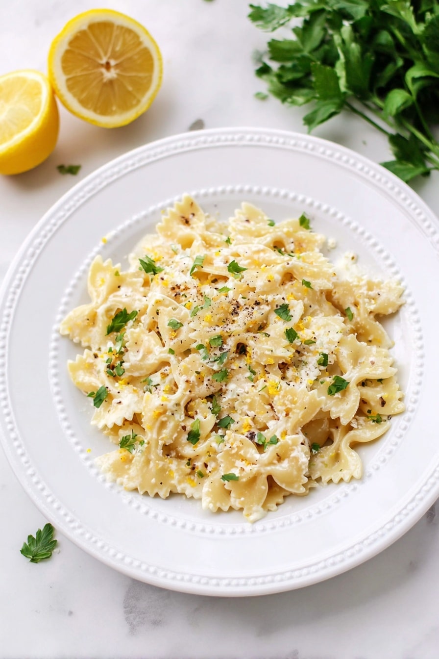 A white round plate with a raised dotted edge holds a single layer of bowtie pasta. The pasta is pale yellow, coated with a creamy white sauce mixed with small bits of cheese and scattered green herb pieces. The dish is lightly sprinkled with cracked black pepper and tiny zest bits of lemon. In the background, two lemon halves are placed on the white marbled surface to the upper left, and a bunch of fresh green parsley lies to the upper right side, also on the white marbled texture. Photo taken with an iphone --ar 2:3 --v 7 - Creamy Lemon Ricotta Pasta, quick lemon ricotta pasta, easy 10-minute pasta recipe, homemade lemon ricotta pasta, fast creamy pasta dish