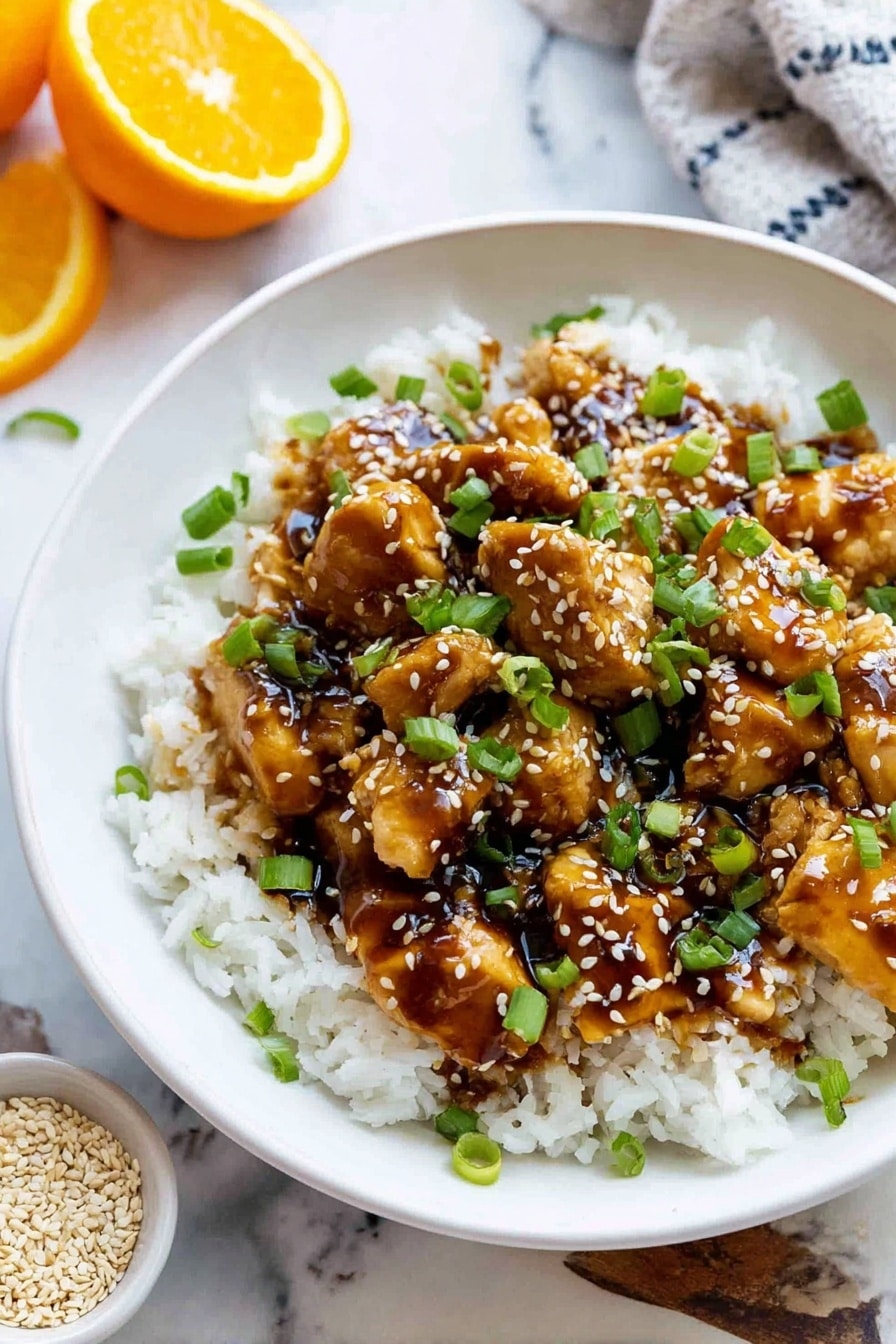 A white bowl filled with two main layers: the bottom layer is fluffy white rice with a soft texture, and on top there are small pieces of golden-brown chicken covered in a shiny, thick dark brown sauce. The dish is sprinkled with light tan sesame seeds and bright green chopped scallions evenly spread over the chicken and rice. The bowl sits on a white marbled surface, with a half-cut orange and a small white bowl of sesame seeds near it. Photo taken with an iphone --ar 2:3 --v 7 - Air Fryer Orange Chicken, healthy orange chicken recipe, quick weeknight dinner, crispy orange chicken, homemade orange chicken