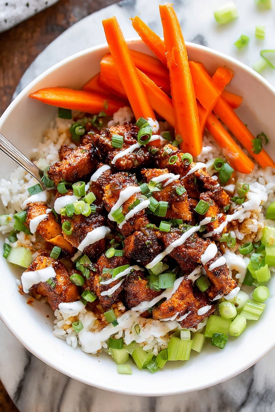 A white bowl holds a layered dish that starts with a base of white rice mixed with small pieces of green celery scattered around. On top, there are dark brown, seasoned chicken pieces arranged in the center, with a few bright orange carrot sticks placed upright on one side. The dish is drizzled with white sauce in thin lines and sprinkled with chopped green onions, adding pops of fresh green color on top. The bowl sits on a white marbled surface, and a metal spoon is partially visible inside the bowl. Photo taken with an iphone --ar 2:3 --v 7 - Crispy Buffalo Chicken Bowls, buffalo chicken bowls healthy, spicy chicken bowls recipe, easy buffalo chicken dinner, homemade buffalo chicken bowls