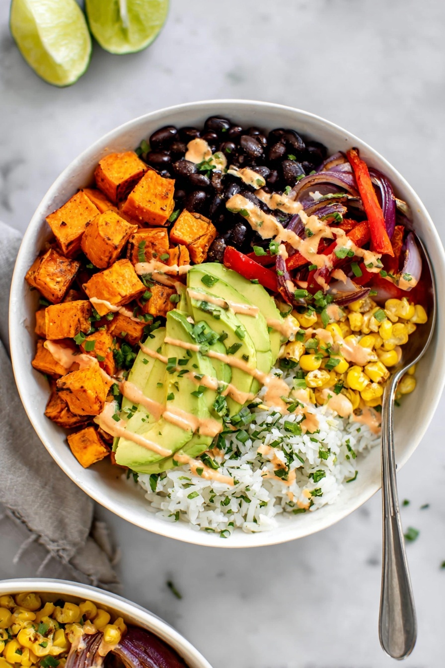 Vegan Sweet Potato Burrito Bowl Recipe 5 A white bowl filled with five main layers arranged in sections: bright orange cubes of roasted sweet potatoes in the top left, shiny black beans in the top right, sautéed red bell pepper strips and purple onion slices in the right middle, fluffy white rice with green herbs mixed in at the bottom right, and grilled yellow corn kernels at the bottom left. On top of the corn and rice, several slices of fresh green avocado are laid. Light orange creamy sauce is drizzled over the avocado, sweet potatoes, beans, and peppers, with small green chive pieces sprinkled on top. The bowl sits on a white marbled surface with lime wedges visible near the top edge. A silver spoon is placed inside the bowl, resting near the rice and avocado. photo taken with an iphone --ar 2:3 --v 7 - Vegan Sweet Potato Burrito Bowl, healthy vegan burrito bowl, plant-based sweet potato bowl, vegan dinner ideas, easy vegan lunch
