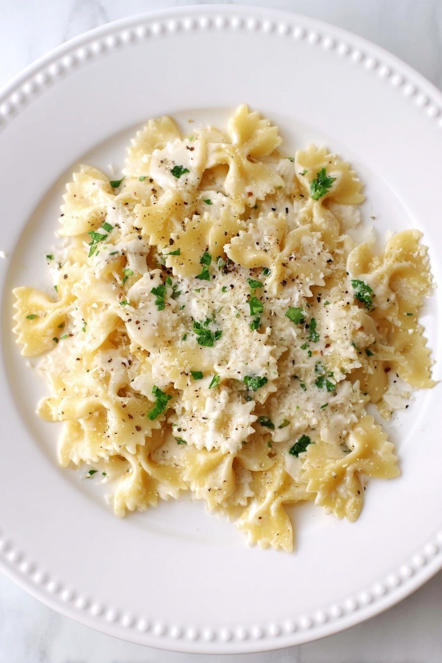 A white plate with a dotted rim holds a single layer of bow-tie pasta covered in a creamy white sauce. The sauce has a slightly grainy texture with small green parsley pieces scattered throughout. There are black pepper specks and fine shreds of cheese on top of the pasta. The dish sits on a white marbled surface. photo taken with an iphone --ar 2:3 --v 7 - Creamy Lemon Ricotta Pasta, quick lemon ricotta pasta, easy 10-minute pasta recipe, homemade lemon ricotta pasta, fast creamy pasta dish