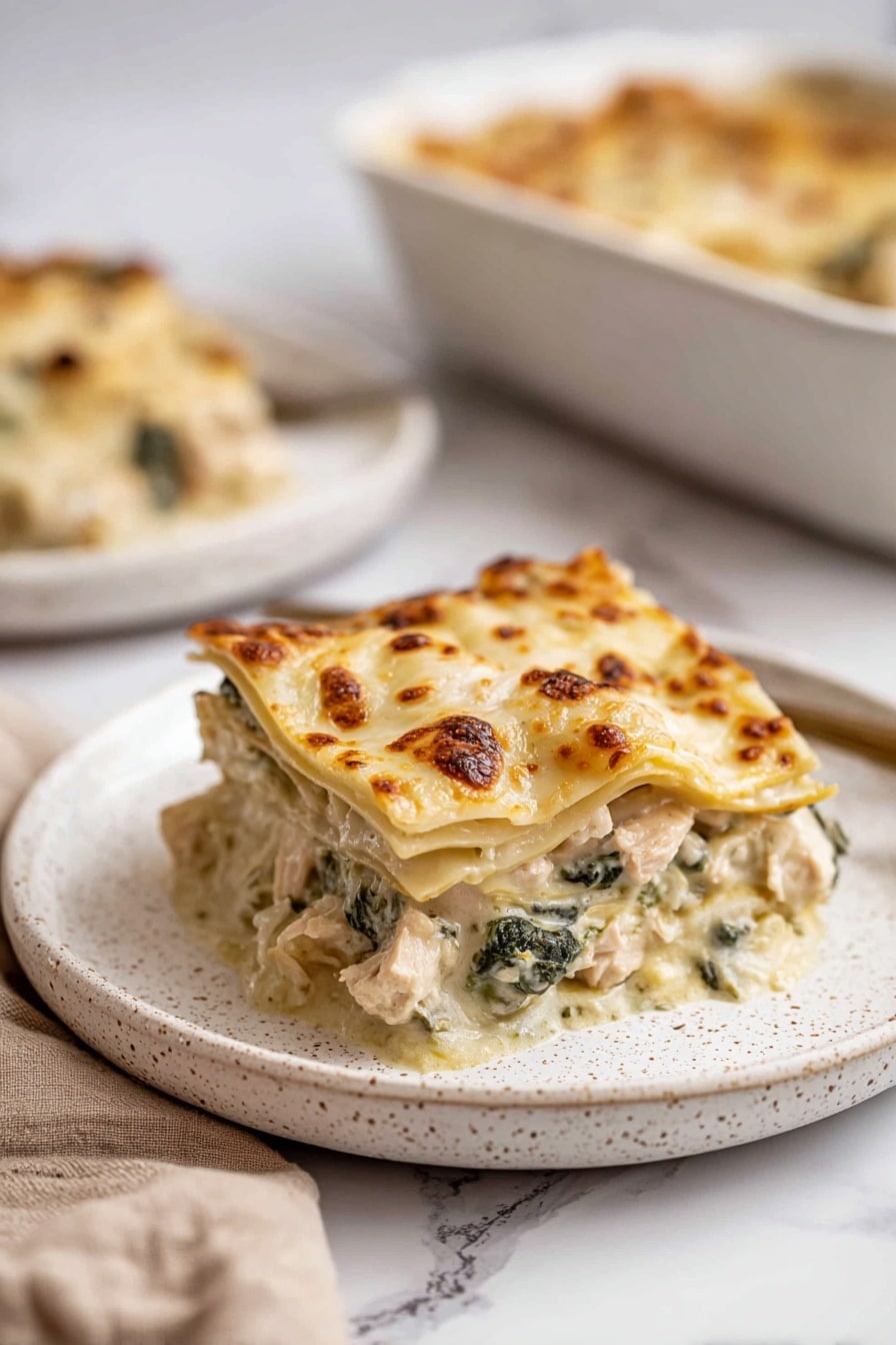 A white rectangular baking dish filled with a lasagna that has a golden brown bubbly cheese layer on top with some browned spots. The cheese layer shows melted texture with visible sautéed mushrooms and dark green spinach leaves scattered throughout. The edges of the dish show slight baked cheese browning with some browned sauce residue. The lasagna layers underneath the cheese appear creamy and well-cooked, hinting at multiple layers of pasta, sauce, mushrooms, and leafy greens forming a rich, thick casserole. The dish is placed on a white marbled surface surrounded by a blue striped cloth on the left, a silver fork and spoon on the top, and two white speckled plates on the bottom and right. Photo taken with an iphone --ar 2:3 --v 7 - Creamy White Chicken Lasagna, white chicken lasagna recipe, easy creamy chicken lasagna, homemade white chicken lasagna, comforting chicken lasagna