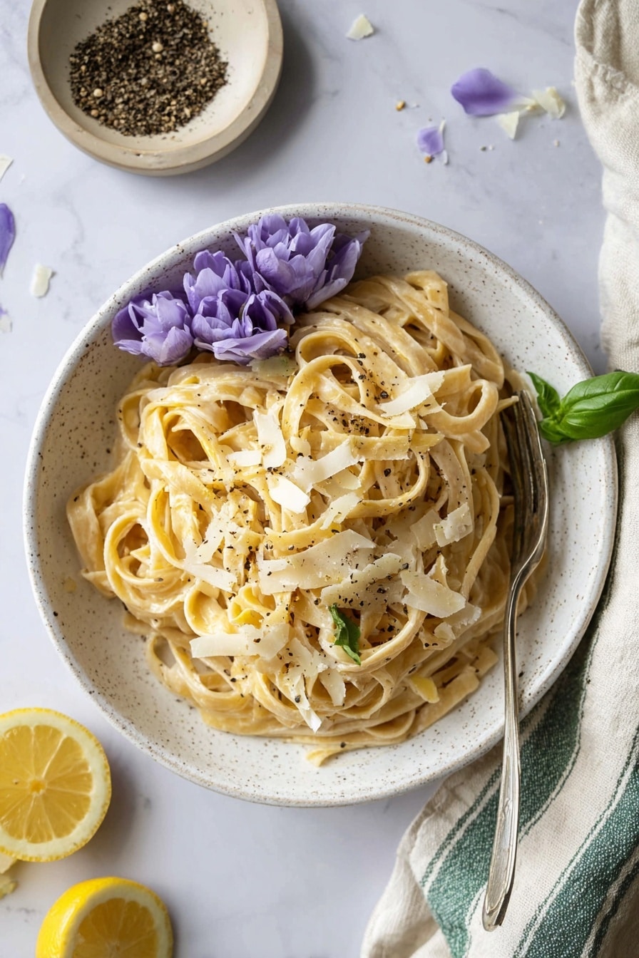 A close-up image of creamy pasta in a white bowl on a white marbled surface, showing twisted layers of light beige fettuccine noodles coated with a smooth, creamy sauce. The pasta is sprinkled with small black pepper bits scattered evenly on top. Thin, pale yellow cheese slices are mixed within the pasta layers, and a small green herb leaf decorates the bottom corner. A purple flower rests on the upper left edge of the bowl, adding a soft pop of color. Photo taken with an iphone --ar 2:3 --v 7 - One Pot Fettuccine Alfredo, easy creamy pasta, quick weeknight dinner, one pot pasta recipe, homemade Alfredo sauce