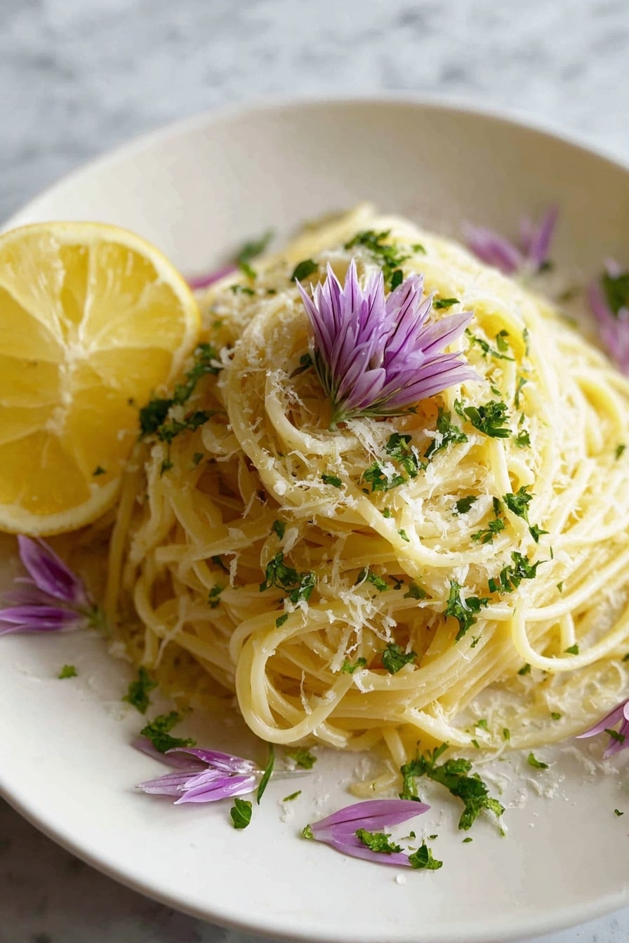 A white plate holds a nest of light yellow spaghetti pasta as the base layer. The pasta is sprinkled with finely grated pale yellow cheese, creating a soft textured layer on top. Bright green parsley leaves are scattered across, adding a fresh, leafy layer. On one side of the pasta, a thin slice of yellow lemon rests lightly, layered with delicate purple flower petals placed beside it. The plate is set on a white marbled surface. Photo taken with an iphone --ar 2:3 --v 7 - One Pot Lemon Pasta, Lemon Pasta Recipe, Easy Lemon Pasta, Quick Pasta Dinner, Fresh Lemon Pasta