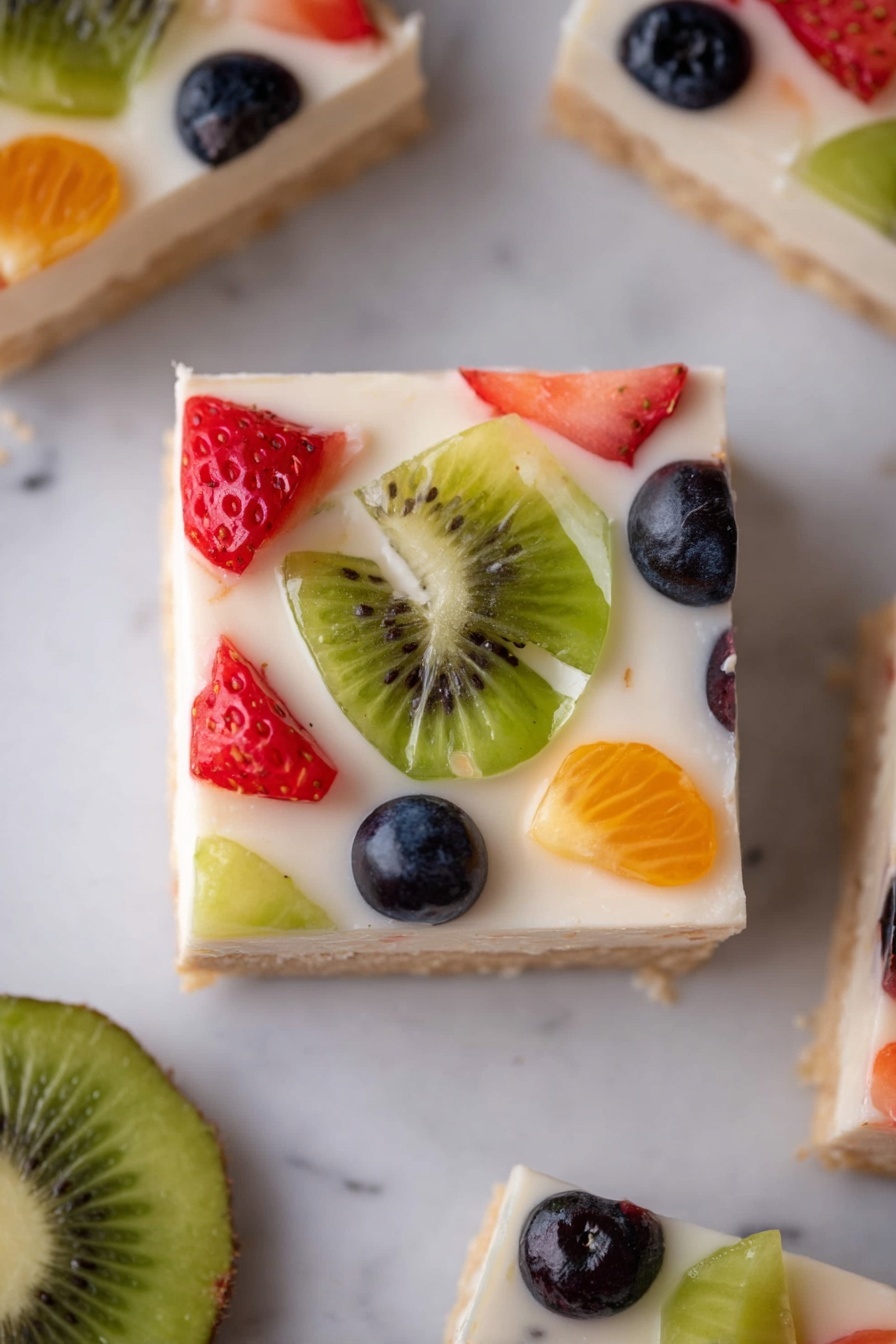 Sugar Cookie Fruit Pizza Bars — The Easiest Summer Dessert Everyone Goes Crazy For! Recipe 7 The image shows a square piece of dessert with three layers: a light brown base, a smooth white creamy middle layer, and a top layer dotted with colorful fruit pieces, including green kiwi slices, red strawberries, dark blue blueberries, and small orange fruit bits. The dessert is placed on a white marbled surface, with a green kiwi slice lying beside it and parts of other similar pieces visible around. The fruity topping looks fresh and shiny, spaced evenly over the creamy layer. photo taken with an iphone --ar 2:3 --v 7 - Sugar Cookie Fruit Pizza Bars, Summer Fruit Dessert, Easy Fruit Pizza Bars, No-Bake Fruit Bars, Fresh Fruit Cookie Bars