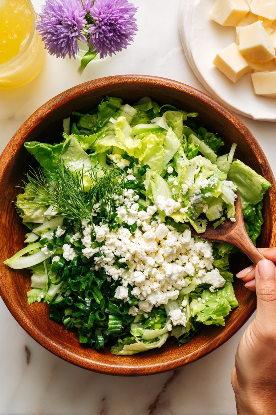 Greek Lettuce Salad with Feta, Dill, and Lemon Recipe 7 A wooden bowl filled with a fresh green salad, which has three main layers: the bottom layer is light green chopped lettuce, the middle layer shows bright green chopped celery, and the top layer is sprinkled with white crumbly cheese and fresh green dill herbs. Around the bowl on a white marbled surface, there is a small gray plate with a block of cheese partially crumbled, a glass of yellow-orange juice, and small purple and white edible flower petals. Photo taken with an iphone --ar 2:3 --v 7 - Greek Lettuce Salad with Feta, Dill, and Lemon, Mediterranean Salad, Easy Greek Salad Recipe, Fresh Lettuce Salad, Summer Salad Ideas
